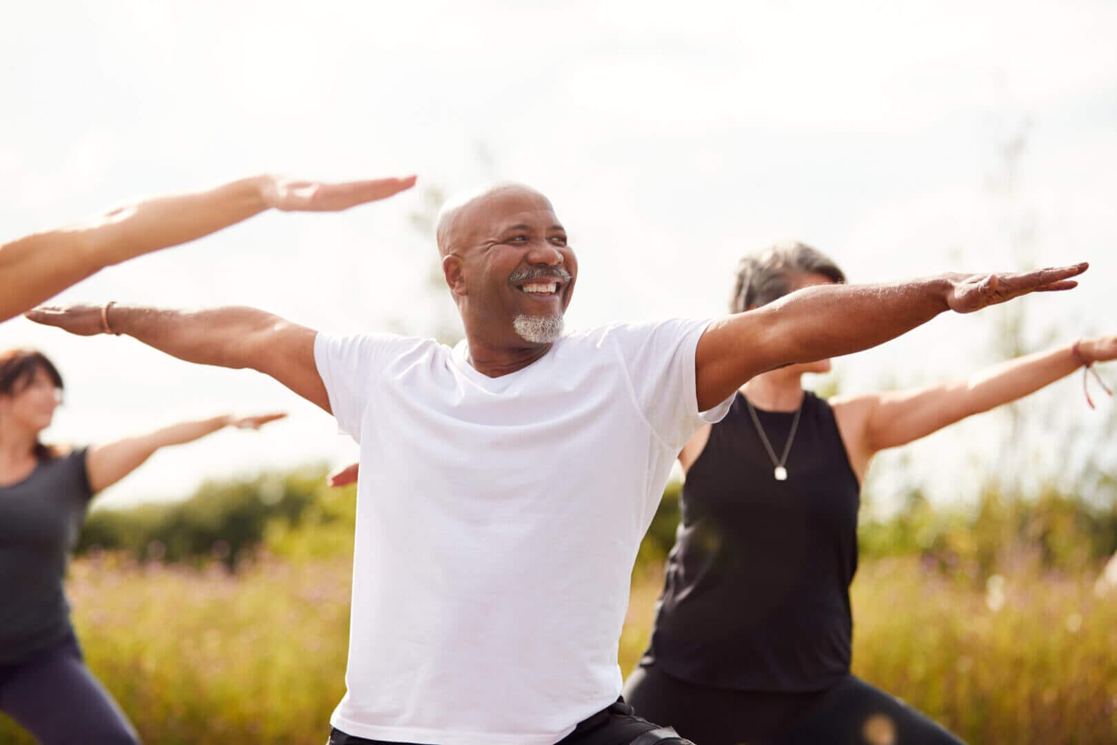 Mature adults practicing yoga outdoors, smiling and stretching at a retreat.
