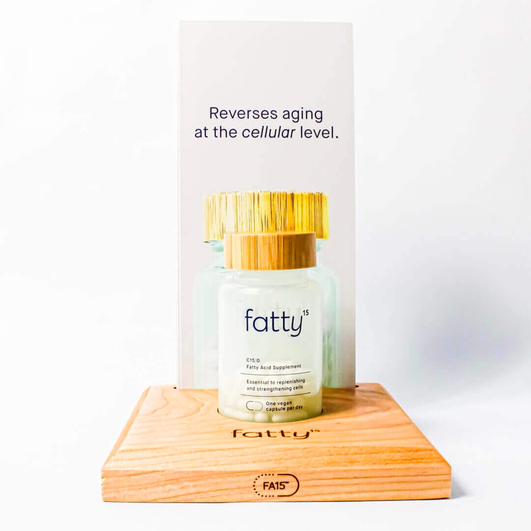 Fatty15 supplement bottle on wooden stand, cellular anti-aging formula, vegan capsules, gold cap, health and wellness product.