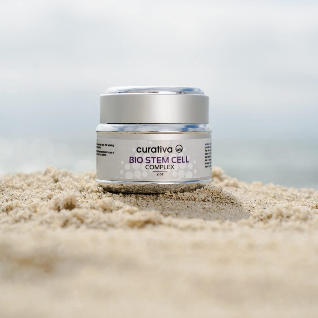 Curativa Bio Stem Cell Complex jar on sandy beach, premium skincare product, anti-aging formula, 2 oz container.