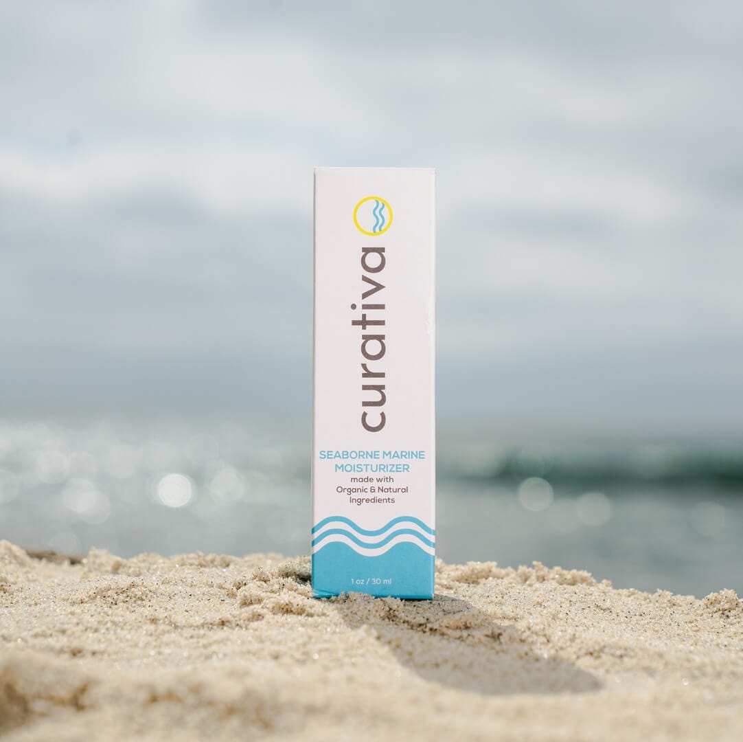Curativa Seaborne Marine Moisturizer on sandy beach, organic skincare, natural ingredients, ocean backdrop.