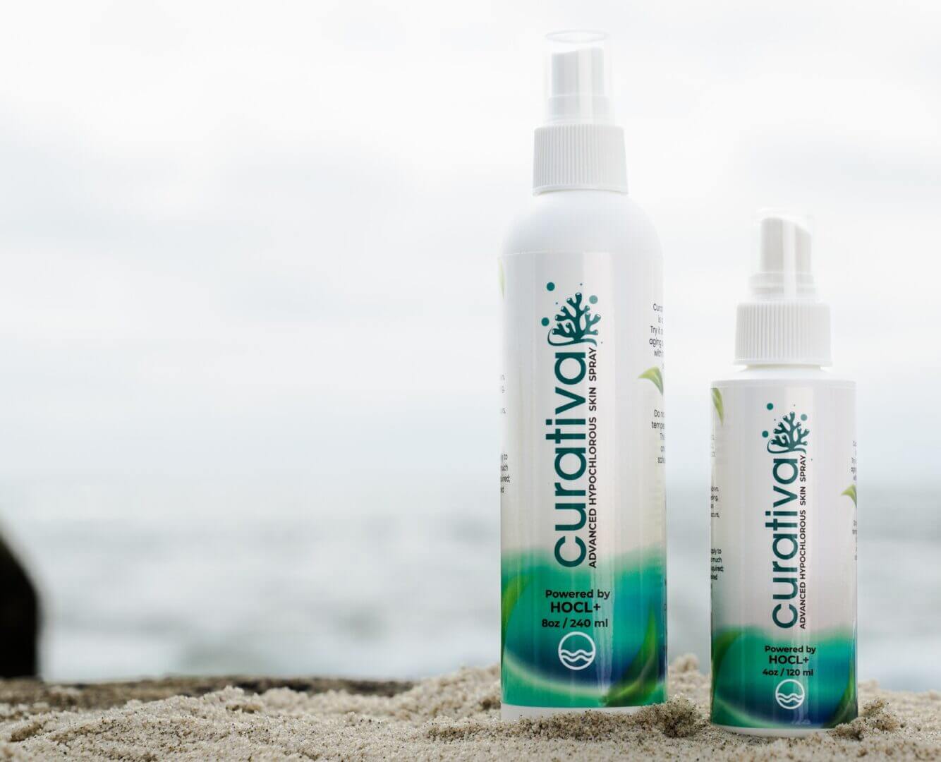 Curativa advanced hypochlorous skin spray bottles on sandy beach, natural skincare, HOCL+, soothing skin treatment.